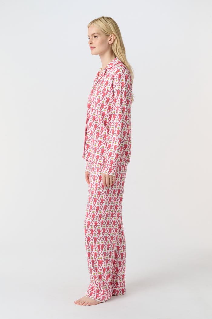 A woman stands barefoot in Roller Rabbit’s Monkey Long Sleeve Polo Pajamas—a matching pink and white Pima cotton set with long sleeves and pants—against a plain white background.