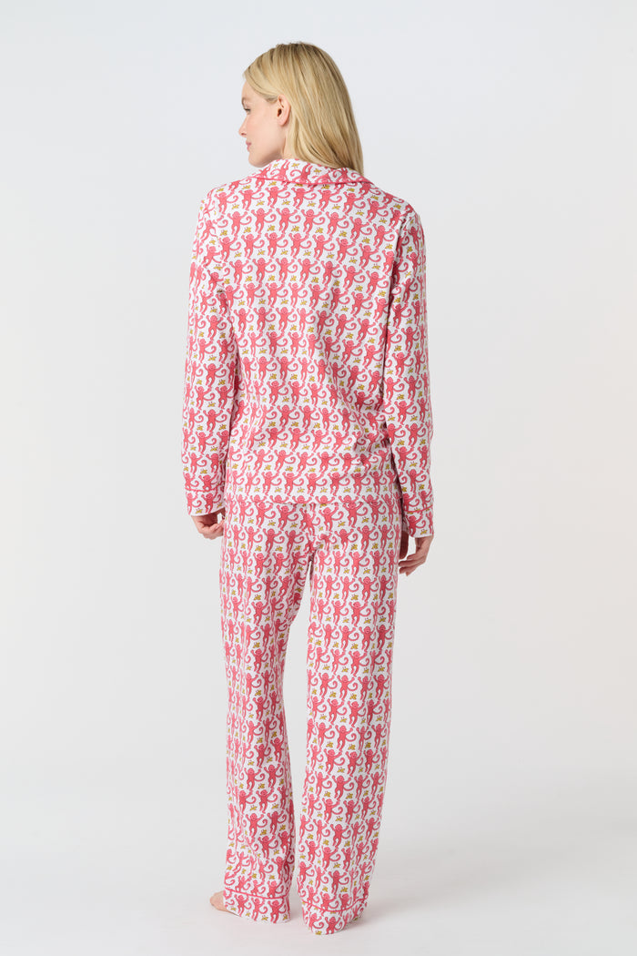 A woman stands barefoot in Roller Rabbit’s Monkey Long Sleeve Polo Pajamas—a matching pink and white Pima cotton set with long sleeves and pants—against a plain white background.