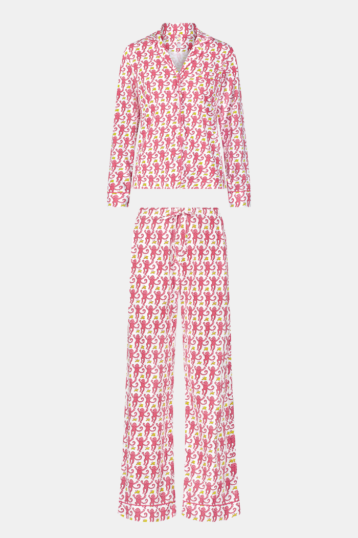 A woman stands barefoot in Roller Rabbit’s Monkey Long Sleeve Polo Pajamas—a matching pink and white Pima cotton set with long sleeves and pants—against a plain white background.