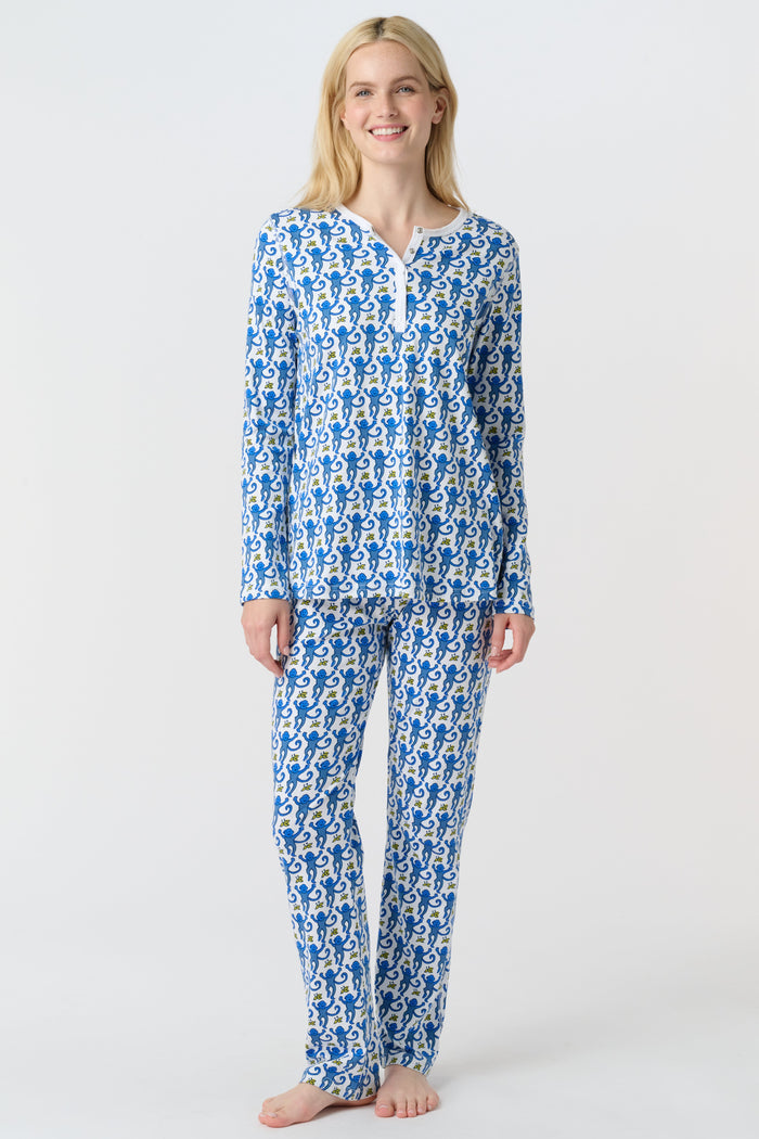 A woman smiles barefoot against a plain white background, wearing Roller Rabbit’s Monkey Pajamas—a matching Pima cotton top and bottom set with a blue and white leafy pattern.