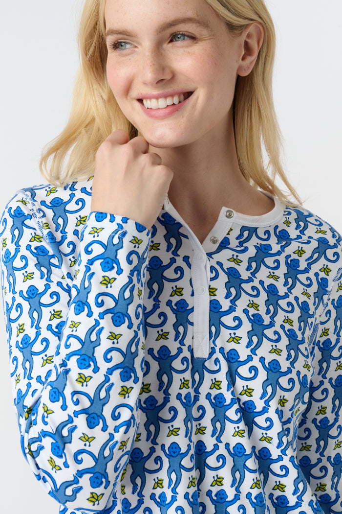 A woman smiles barefoot against a plain white background, wearing Roller Rabbit’s Monkey Pajamas—a matching Pima cotton top and bottom set with a blue and white leafy pattern.