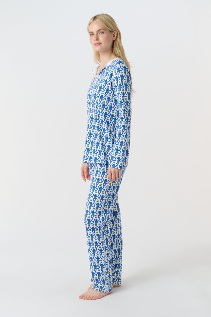 A woman smiles barefoot against a plain white background, wearing Roller Rabbit’s Monkey Pajamas—a matching Pima cotton top and bottom set with a blue and white leafy pattern.