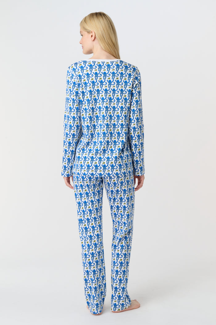 A woman smiles barefoot against a plain white background, wearing Roller Rabbit’s Monkey Pajamas—a matching Pima cotton top and bottom set with a blue and white leafy pattern.