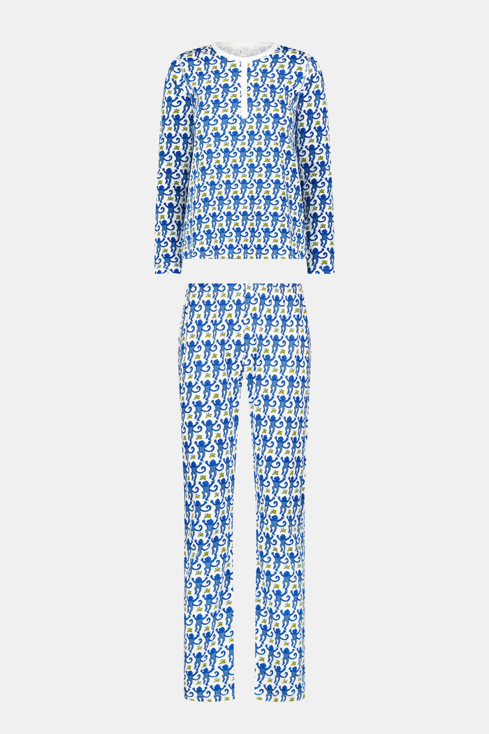A woman smiles barefoot against a plain white background, wearing Roller Rabbit’s Monkey Pajamas—a matching Pima cotton top and bottom set with a blue and white leafy pattern.