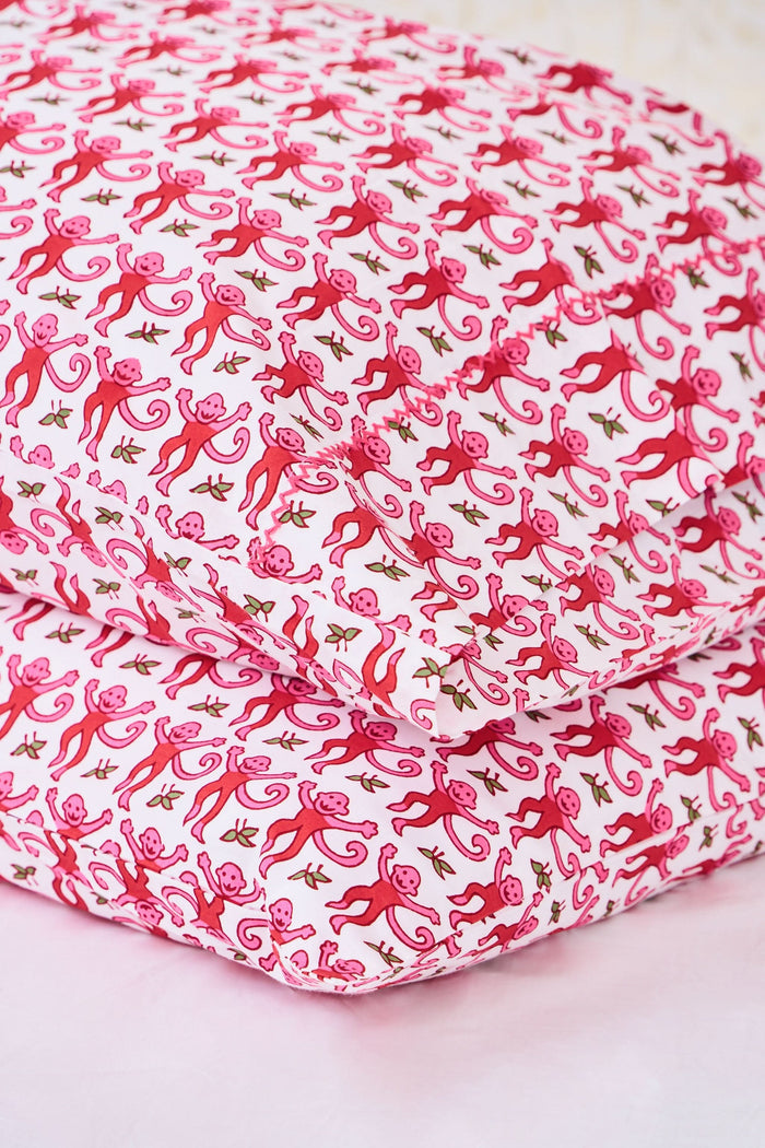 Two stacked pillows are covered with Roller Rabbit’s Monkey Pillowcase Set, featuring a playful pink monkey print with leaves. The whimsical pattern repeats across the entire surface, creating a charming and cheerful bedding look.