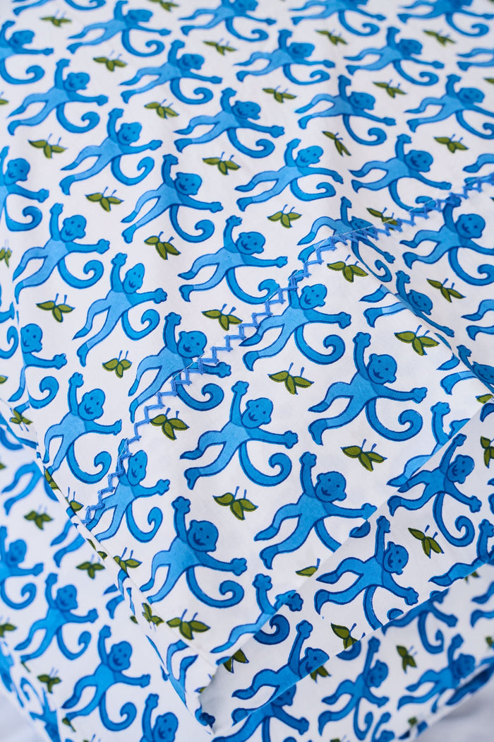 Two Monkey Pillowcase Set pillows by Roller Rabbit, featuring a blue and green floral pattern and 100 cotton pillowcases, are stacked on a white surface with a cream decorative screen in the background.