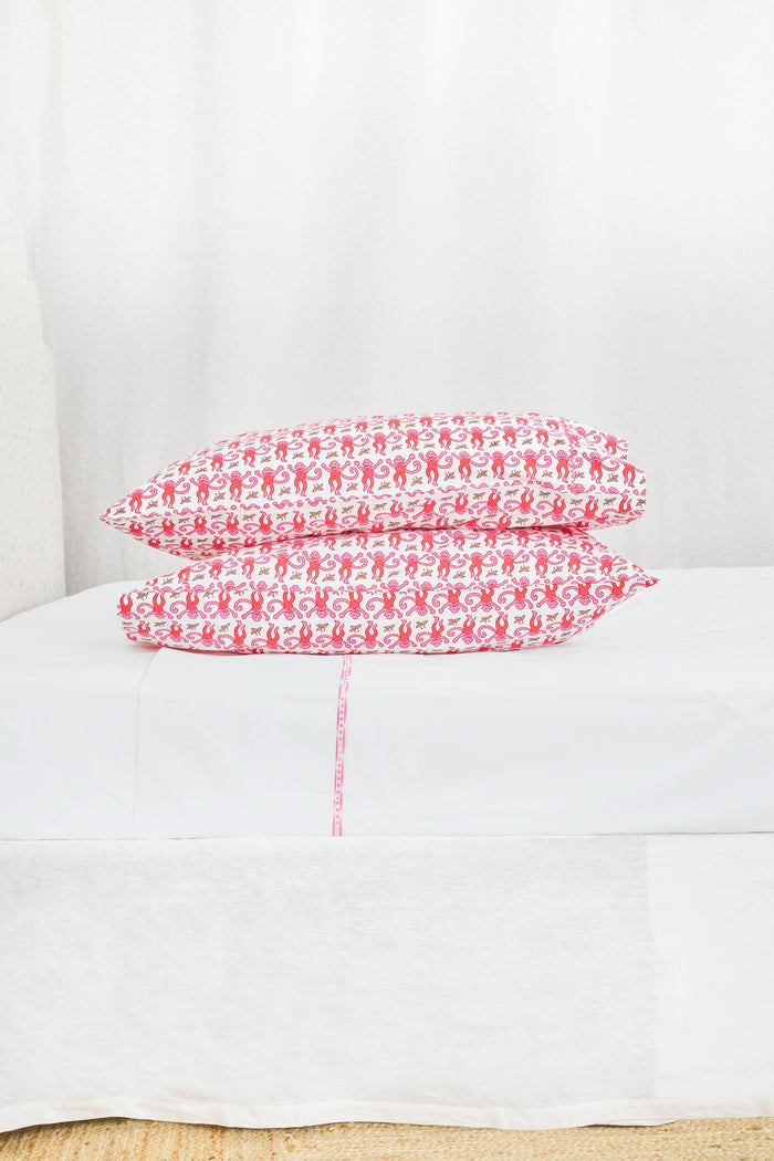 Two stacked pillows are covered with Roller Rabbit’s Monkey Pillowcase Set, featuring a playful pink monkey print with leaves. The whimsical pattern repeats across the entire surface, creating a charming and cheerful bedding look.