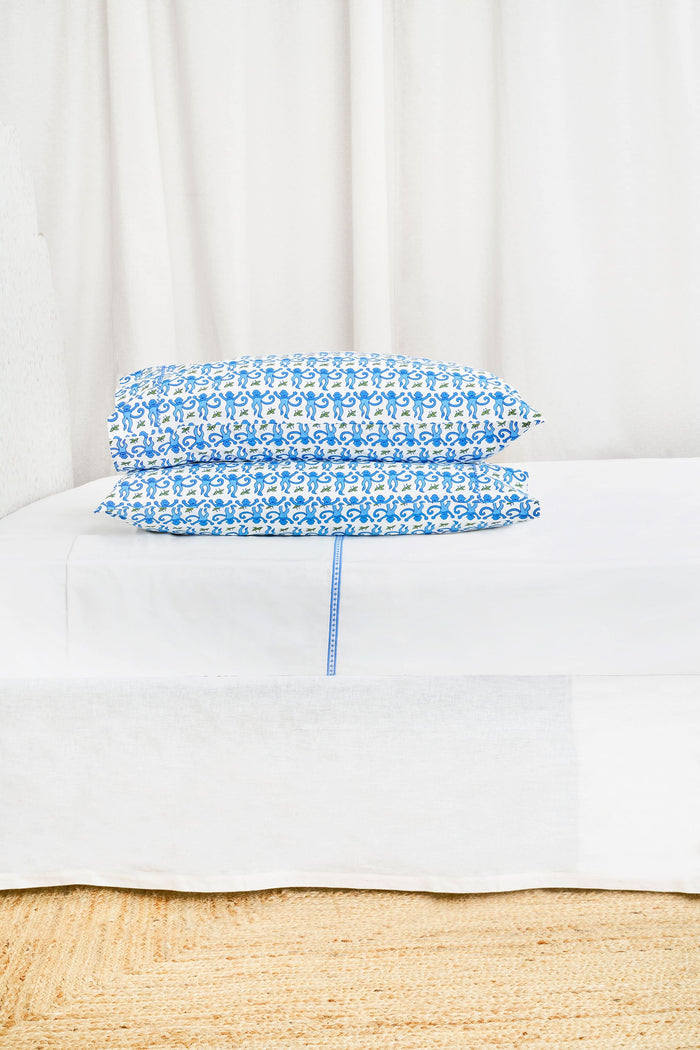 Two Monkey Pillowcase Set pillows by Roller Rabbit, featuring a blue and green floral pattern and 100 cotton pillowcases, are stacked on a white surface with a cream decorative screen in the background.