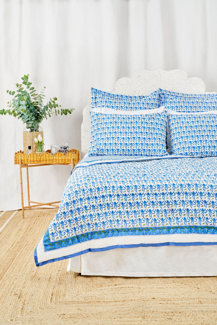 Two Monkey Pillowcase Set pillows by Roller Rabbit, featuring a blue and green floral pattern and 100 cotton pillowcases, are stacked on a white surface with a cream decorative screen in the background.