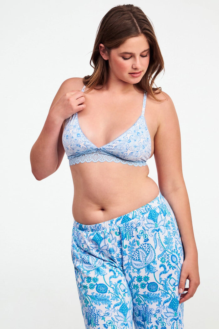 A woman wears the Roller Rabbit Monkey Rosette Mercer Bralette—a light blue triangle bralette with playful monkey print, scalloped lace trim, thin straps, and a V-neck—shown from the chest up.