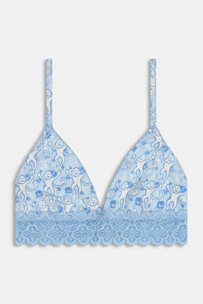 A woman wears the Roller Rabbit Monkey Rosette Mercer Bralette—a light blue triangle bralette with playful monkey print, scalloped lace trim, thin straps, and a V-neck—shown from the chest up.