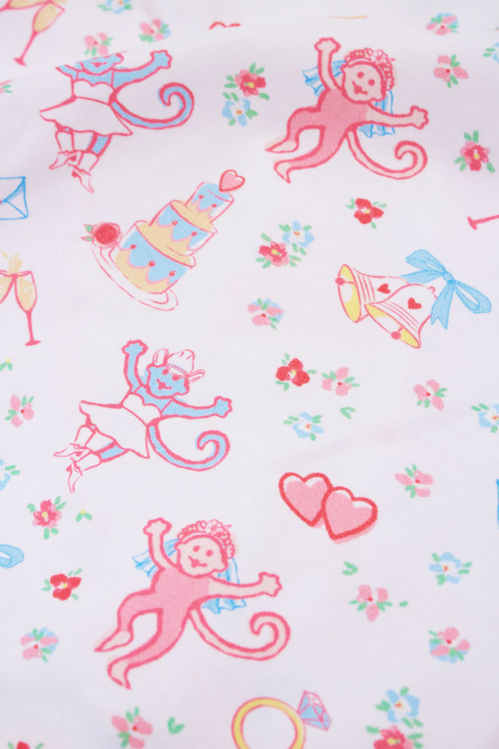 A woman smiles while wearing Roller Rabbit’s Monkey Said Yes Polo Pajamas—a short-sleeved, button-up top and matching shorts with a colorful, playful print featuring whimsical illustrations.