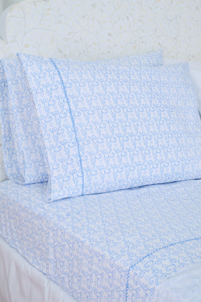 Close up of a white bed with the Roller Rabbit Monkey Sheet Set, featuring light blue monkey-printed cotton sheets and pillowcases.