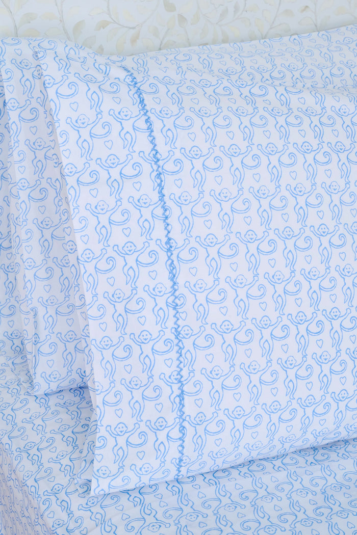 Close up of a white bed with the Roller Rabbit Monkey Sheet Set, featuring light blue monkey-printed cotton sheets and pillowcases.