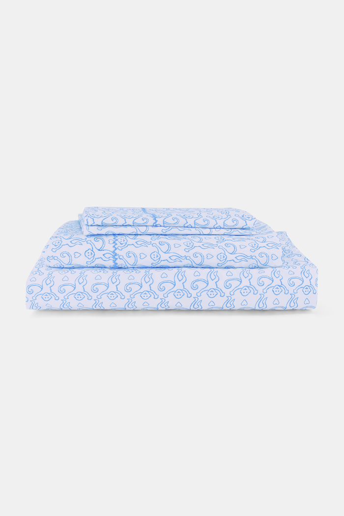 Close up of a white bed with the Roller Rabbit Monkey Sheet Set, featuring light blue monkey-printed cotton sheets and pillowcases.