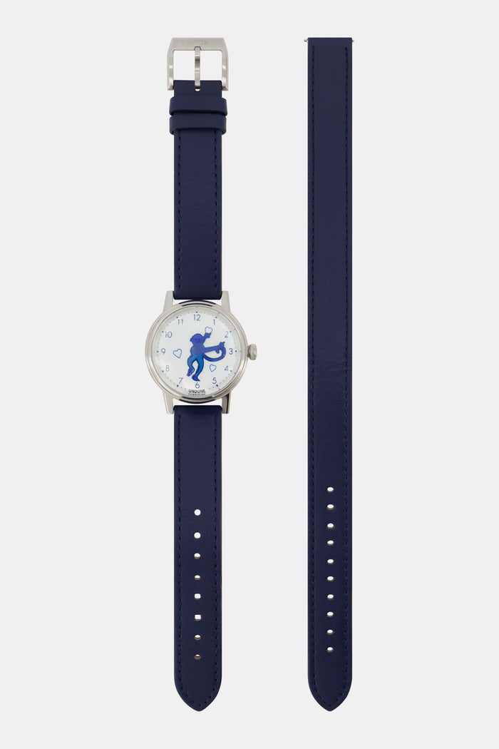 A woman wears a navy blue sweater, a gold heart-shaped pendant necklace, and the Monkey Watch by Roller Rabbit with an Italian leather strap. She crosses her arm over her chest, highlighting her stylish accessories.