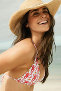A woman wearing the Roller Rabbit Monkey/Hearts Serena Bikini Top and a straw hat smiles happily on a beach with the ocean in the background.