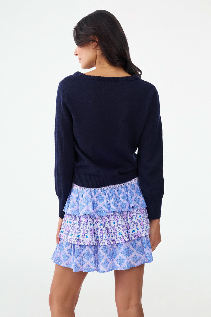 A person wearing a navy long-sleeve top and the Roller Rabbit Monkey/Jemina Siggy Skirt, a tiered ruffle mini with blue and purple floral and leafy patterns. Only the torso and upper legs are visible.