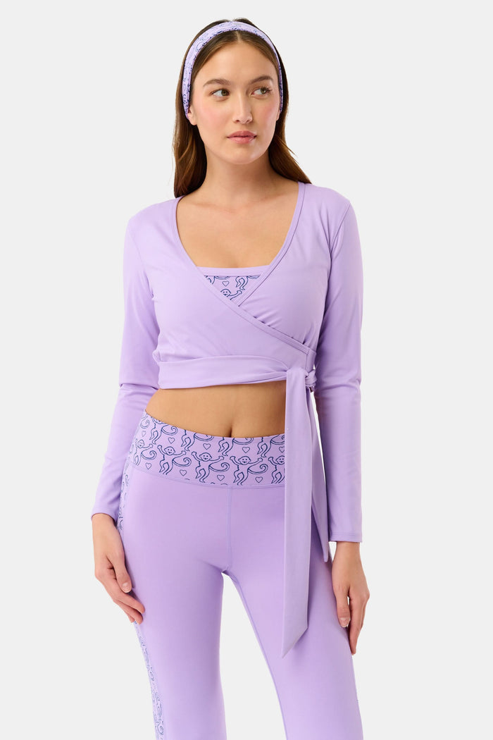 A woman wears the Roller Rabbit Morgan Wrap Top in lavender over a matching blue abstract sports bra, paired with high-waisted leggings in the same print. The photo is cropped from shoulders to waist.