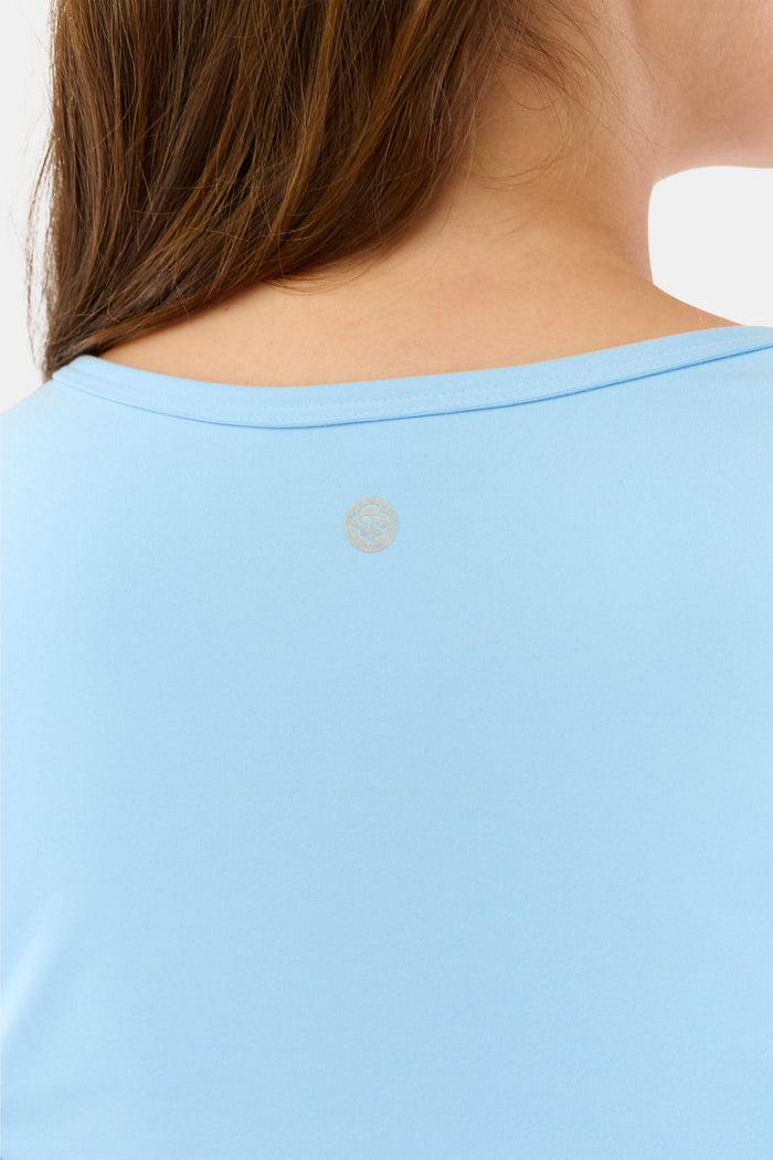 A woman stands facing forward against a plain light background, wearing the Roller Rabbit Morgan Wrap Top in sky blue, paired with high-waisted leggings and a matching headband, modeling stylish women’s activewear.
