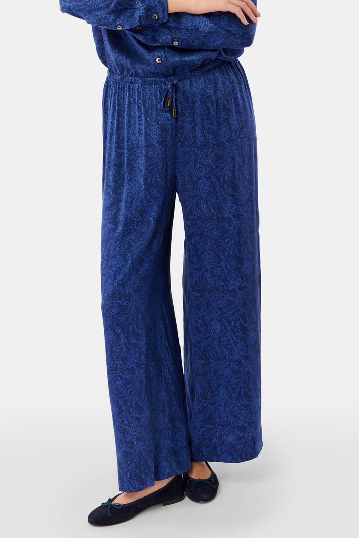 Dressed in Roller Rabbit’s Morris Floral Paige Pant and a matching top, paired with black ballet flats, a person stands against a plain light background.