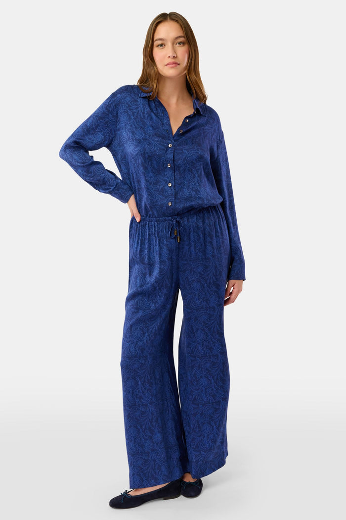 Dressed in Roller Rabbit’s Morris Floral Paige Pant and a matching top, paired with black ballet flats, a person stands against a plain light background.