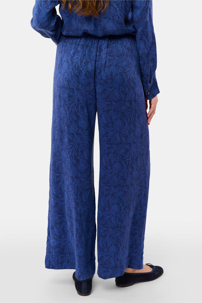 Dressed in Roller Rabbit’s Morris Floral Paige Pant and a matching top, paired with black ballet flats, a person stands against a plain light background.