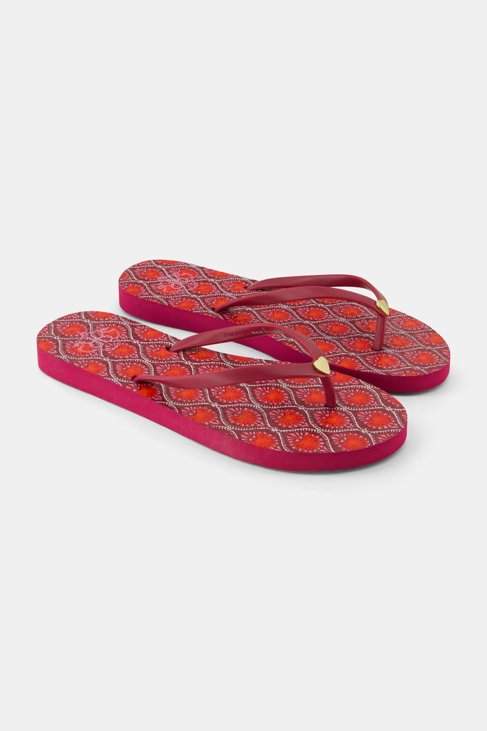 The Roller Rabbit Palm Fronds Flip Flops feature burgundy soles with orange and white geometric patterns, solid red straps with gold accents, and are perfect as swimwear matching sandals. Displayed on a white background.
