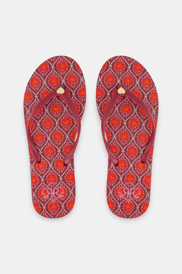 The Roller Rabbit Palm Fronds Flip Flops feature burgundy soles with orange and white geometric patterns, solid red straps with gold accents, and are perfect as swimwear matching sandals. Displayed on a white background.