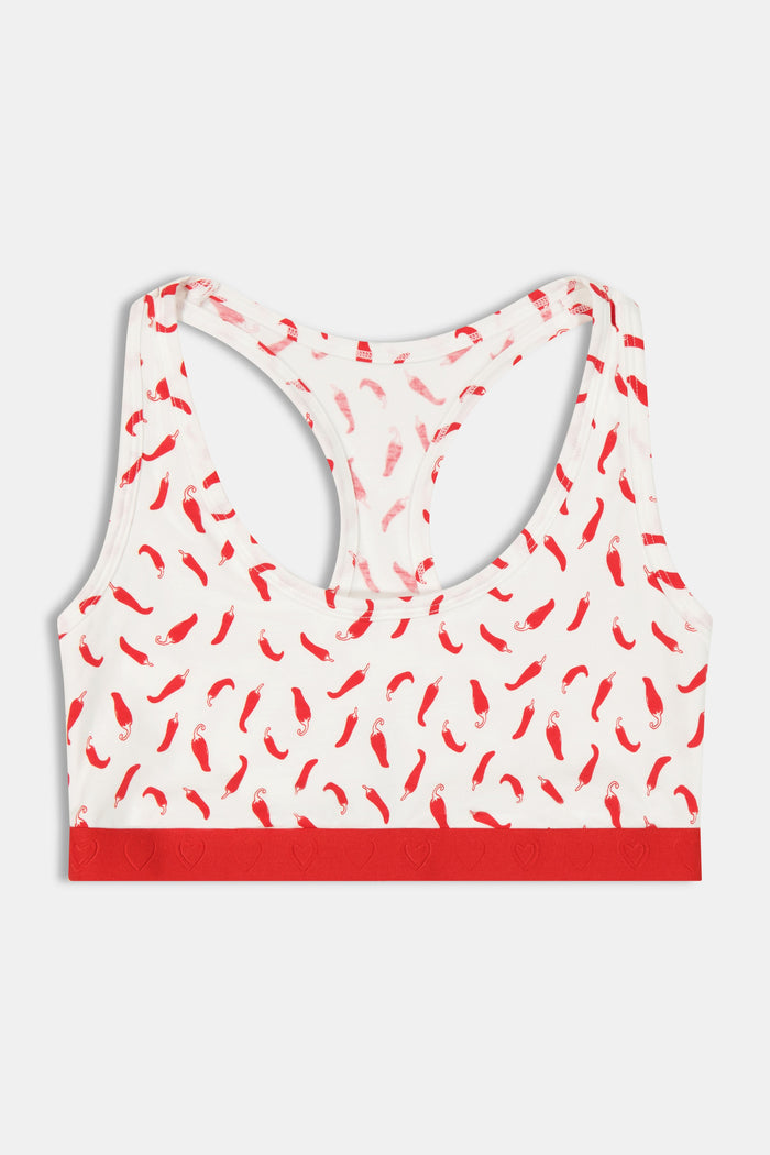 A woman models the Roller Rabbit Picante Madison Racerback Bralette, featuring a cotton-modal blend with a red chili pepper print and red band. The racerback design is shown in a cropped image from shoulders to midriff.