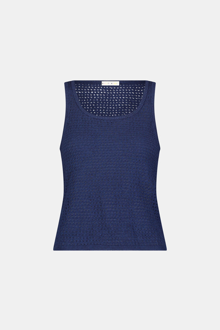 A woman wears the Roller Rabbit Pointelle Sasha Sweater Tank in navy with a textured open-weave design, paired with white shorts featuring blue floral prints. She is shown from shoulders to waist, looking slightly to the side.