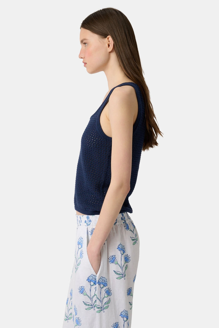 A woman wears the Roller Rabbit Pointelle Sasha Sweater Tank in navy with a textured open-weave design, paired with white shorts featuring blue floral prints. She is shown from shoulders to waist, looking slightly to the side.