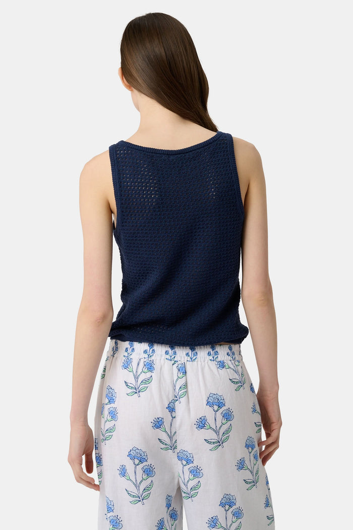 A woman wears the Roller Rabbit Pointelle Sasha Sweater Tank in navy with a textured open-weave design, paired with white shorts featuring blue floral prints. She is shown from shoulders to waist, looking slightly to the side.