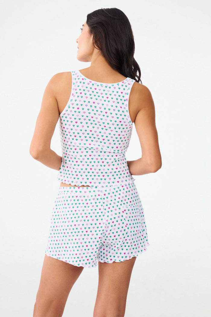 A woman adjusts her Pop Hearts Rib Astor Tank by Roller Rabbit, a sleeveless pajama top with matching shorts, featuring soft pima modal fabric with colorful strawberries on a white background.