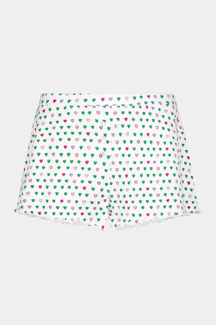 A person models Roller Rabbit's Pop Hearts Rib Sullivan Shortie set—white, super-soft loungewear with small green, blue, and pink hearts and boxer-inspired style—against a plain light background.
