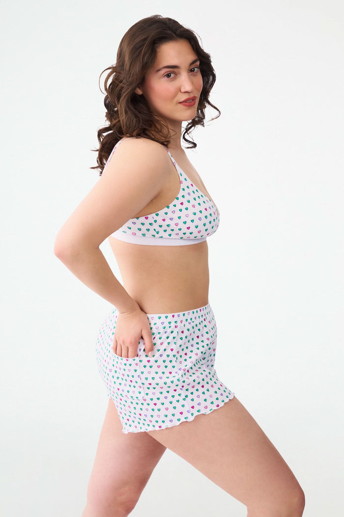 A person models Roller Rabbit's Pop Hearts Rib Sullivan Shortie set—white, super-soft loungewear with small green, blue, and pink hearts and boxer-inspired style—against a plain light background.