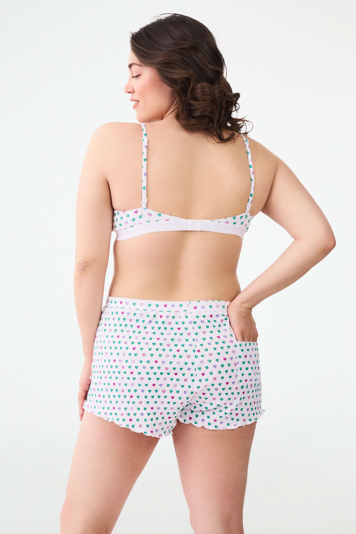 A person models Roller Rabbit's Pop Hearts Rib Sullivan Shortie set—white, super-soft loungewear with small green, blue, and pink hearts and boxer-inspired style—against a plain light background.