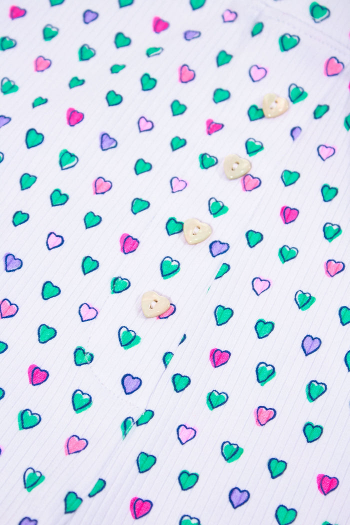 A person models Roller Rabbit's Pop Hearts Rib Sullivan Shortie set—white, super-soft loungewear with small green, blue, and pink hearts and boxer-inspired style—against a plain light background.