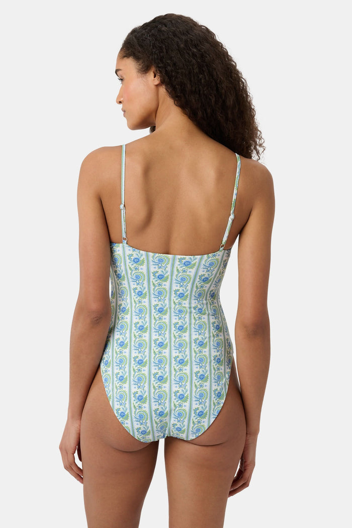 A woman models the Roller Rabbit Provencal Stripe Aurora One Piece, a blue and green vintage-inspired swimsuit with thin straps and a front keyhole, against a white background. This UPF 50+ swimwear combines style and sun protection.
