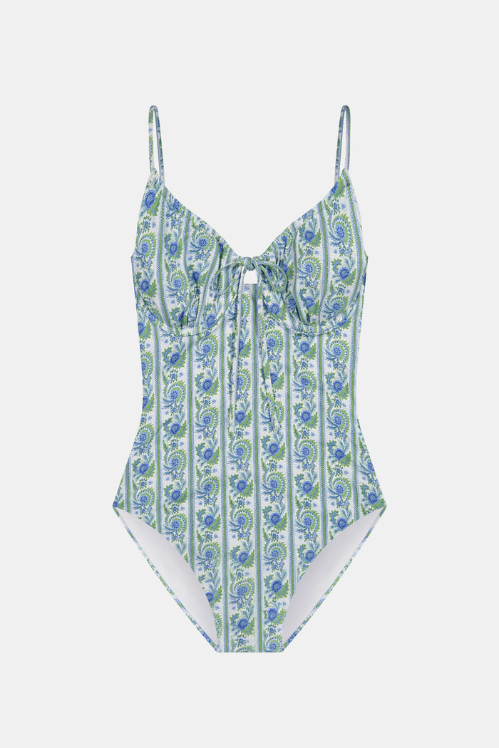 A woman models the Roller Rabbit Provencal Stripe Aurora One Piece, a blue and green vintage-inspired swimsuit with thin straps and a front keyhole, against a white background. This UPF 50+ swimwear combines style and sun protection.