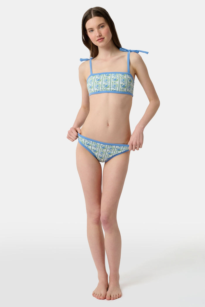 A person shown from the waist to upper thighs is wearing the Roller Rabbit Provencal Stripe Oceana Bikini Bottom featuring a blue and green floral design with light blue trim in a high-waisted bikini style.