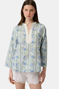A woman models the Roller Rabbit Provencal Stripe Willow Tunic with blue and green floral patterns and a white V-neckline, paired with white scallop-hem shorts, against a plain light background.