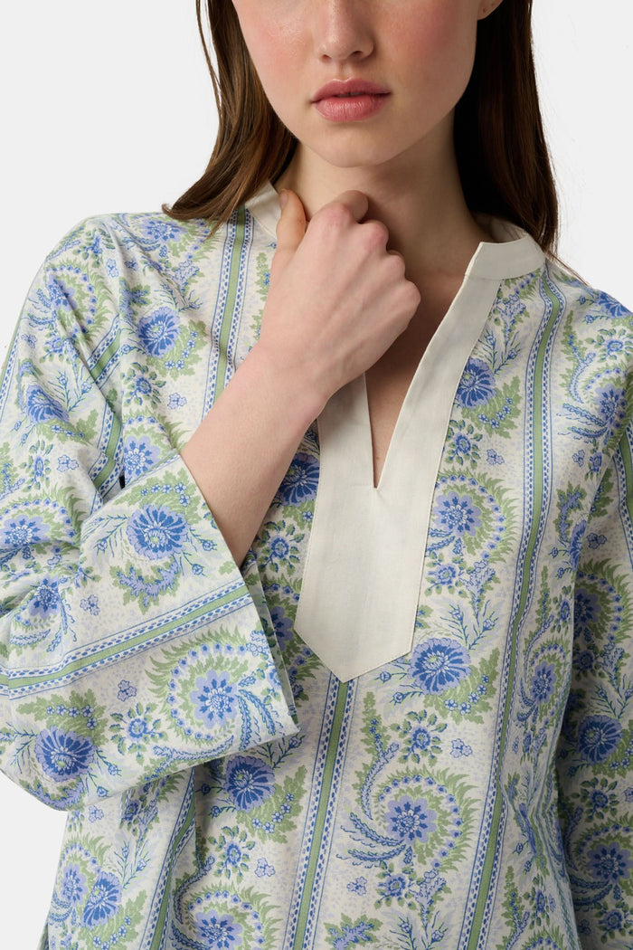 A woman models the Roller Rabbit Provencal Stripe Willow Tunic with blue and green floral patterns and a white V-neckline, paired with white scallop-hem shorts, against a plain light background.