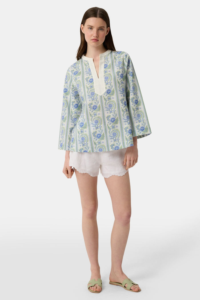 A woman models the Roller Rabbit Provencal Stripe Willow Tunic with blue and green floral patterns and a white V-neckline, paired with white scallop-hem shorts, against a plain light background.