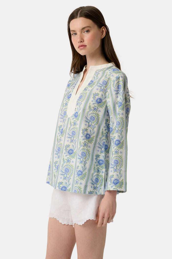 A woman models the Roller Rabbit Provencal Stripe Willow Tunic with blue and green floral patterns and a white V-neckline, paired with white scallop-hem shorts, against a plain light background.