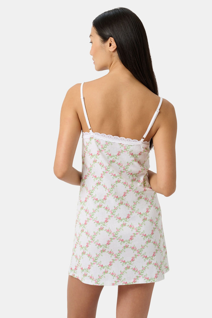 A woman models the Roller Rabbit Raspberry Garden Pearl Slip Dress, with thin straps and a pink bow at the neckline, against a plain light gray background.