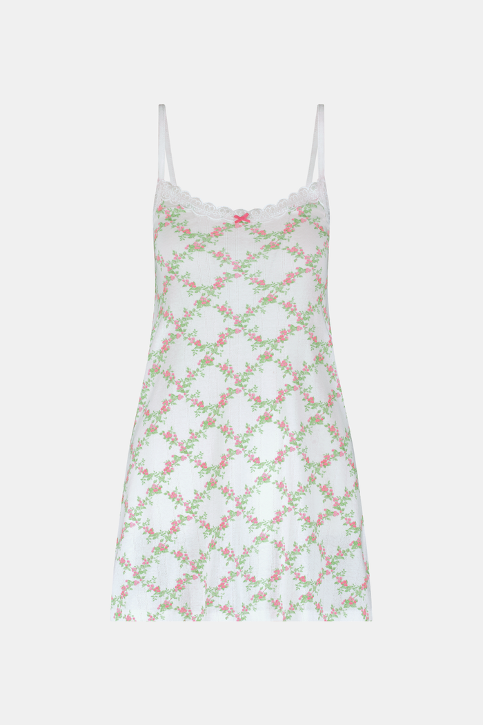 A woman models the Roller Rabbit Raspberry Garden Pearl Slip Dress, with thin straps and a pink bow at the neckline, against a plain light gray background.