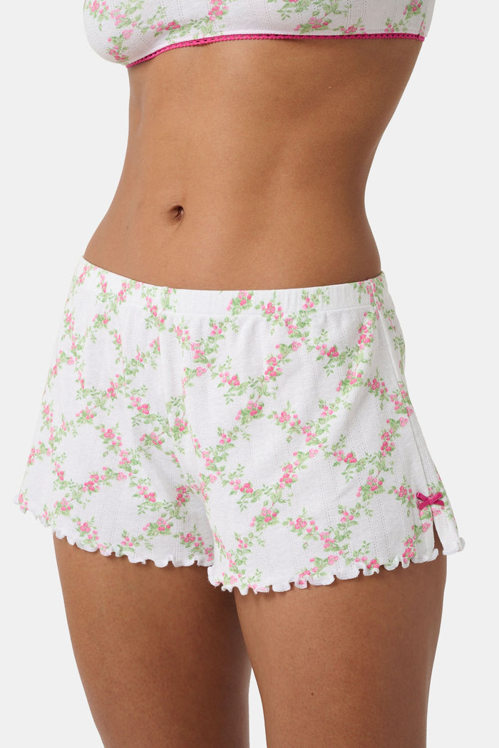 A person wearing Roller Rabbit Raspberry Garden Tara Shorts with a pink bow detail and a matching crop top, both in soft Pima Pointelle cotton, showing only their torso and upper thighs against a plain background.