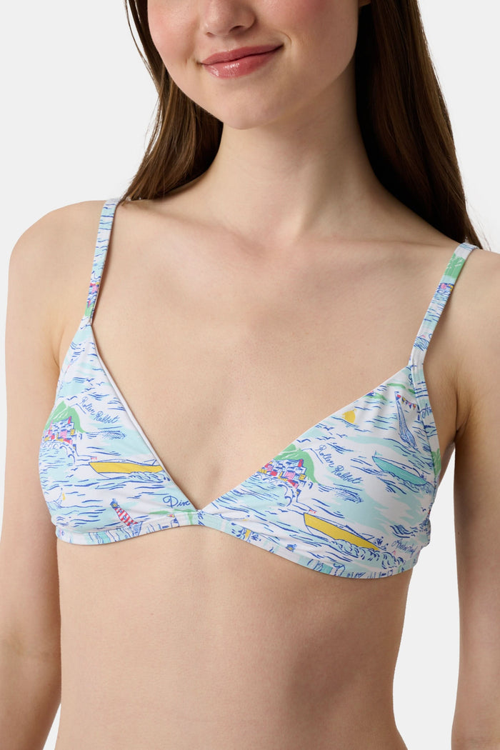 A woman with long brown hair smiles softly, wearing the Regatta Marais Bikini Top by Roller Rabbit in a nautical print, standing against a plain white background.