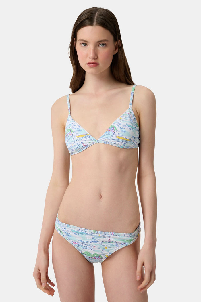 A woman with long brown hair smiles softly, wearing the Regatta Marais Bikini Top by Roller Rabbit in a nautical print, standing against a plain white background.